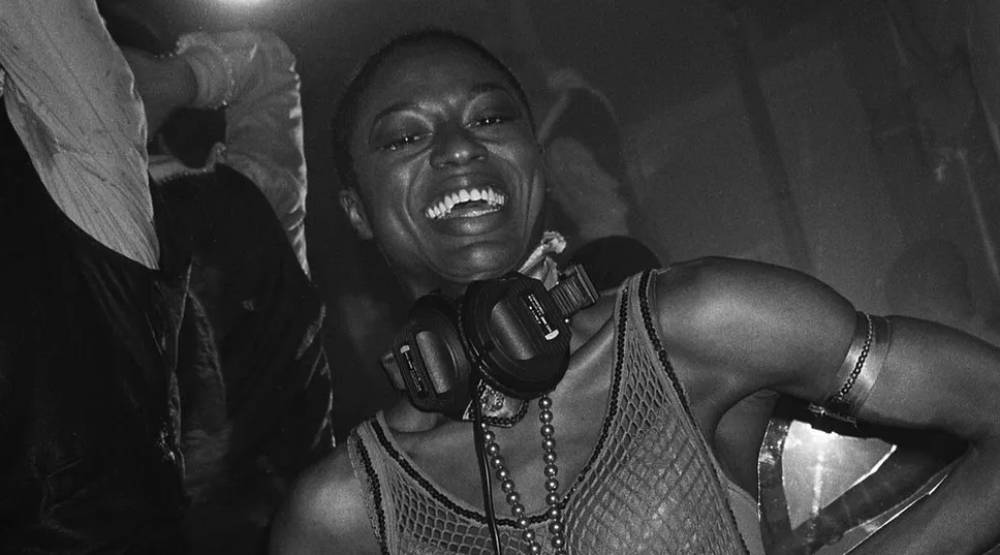 DJ Paulette in a vest with plenty of arm jewellery smiling into camera