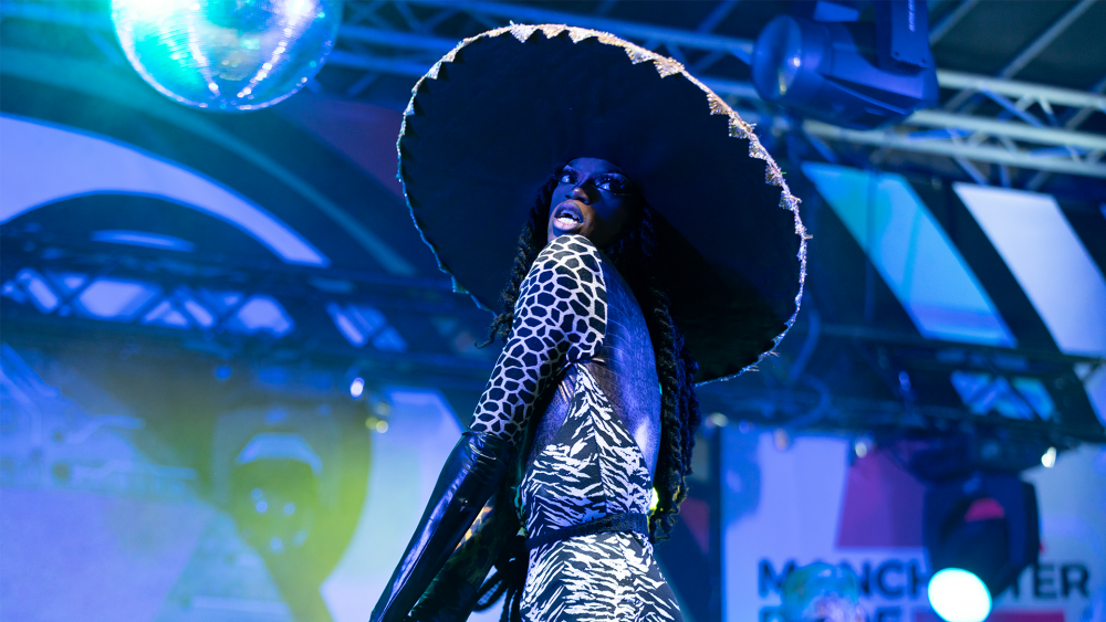 Black Peppa in a black and white leotard, wearing a large, black circular hat sat atop long black braids that are waist length