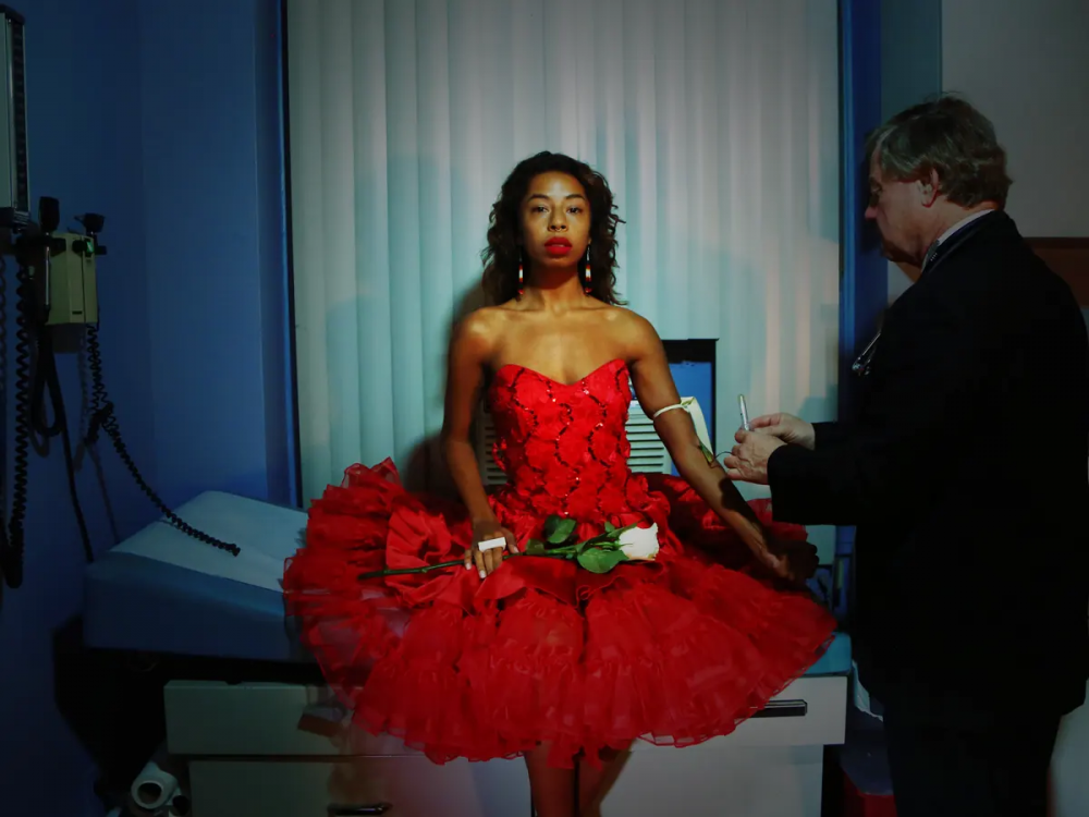 A black woman in a red dress holds a bouquet of white roses