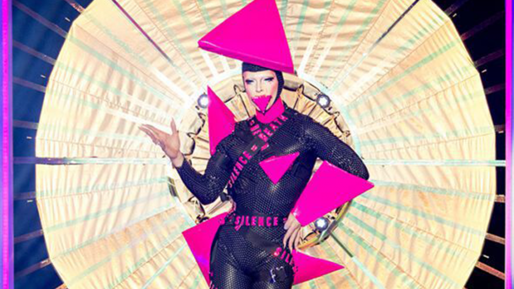 Cheddar Gorgeous in their incredible Drag Race outfit with a black catsuit covered in pink triangles